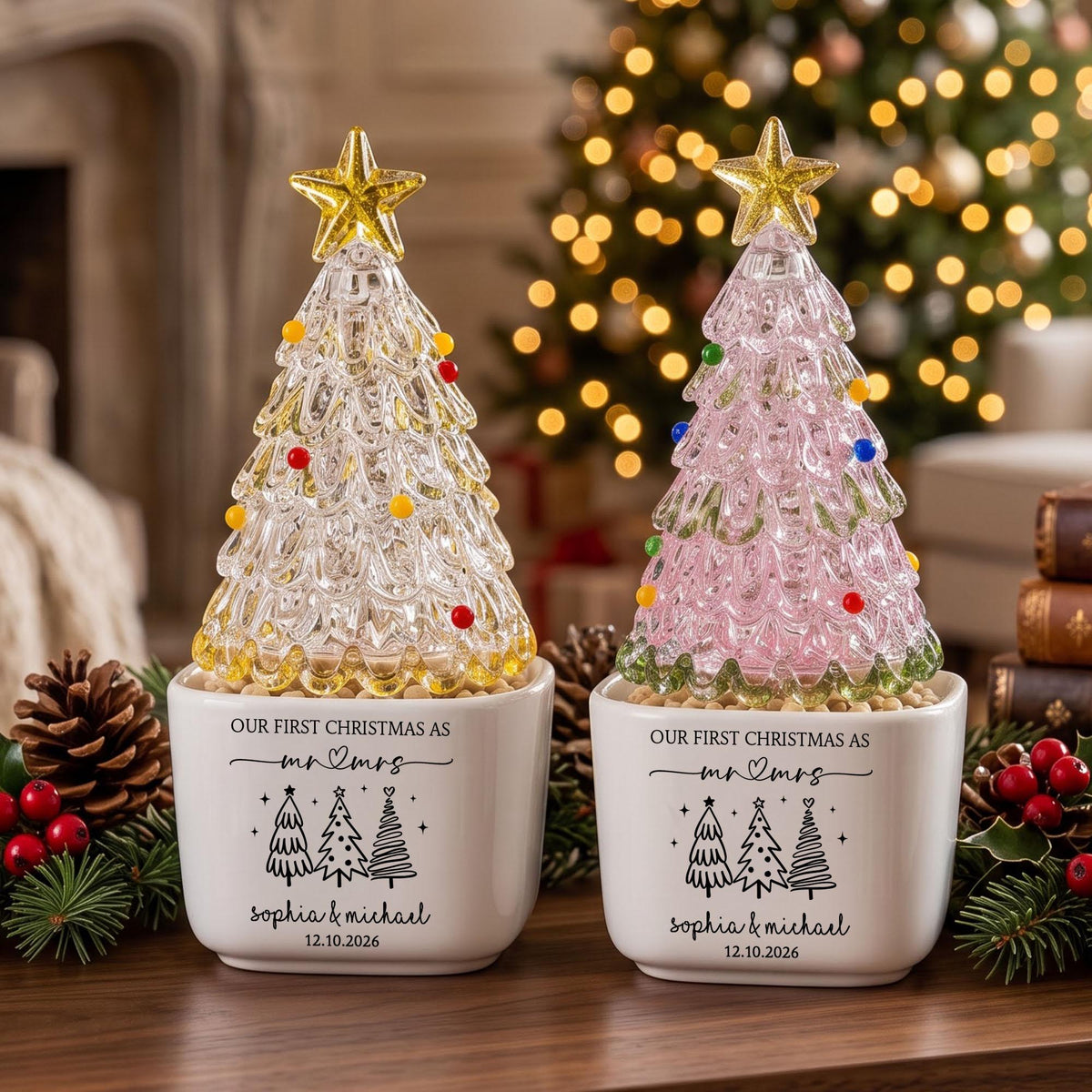May include: Two glass Christmas tree figurines with yellow and pink tints, topped with gold stars and colorful glass ornaments. Each sits in a white square ceramic planter printed with "OUR FIRST CHRISTMAS AS mr & mrs", three tree icons, "Sophia & Michael", and "12.10.2026".