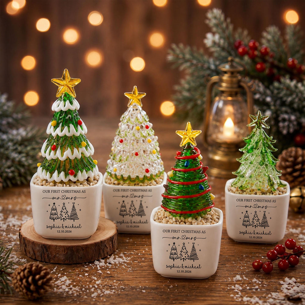 May include: Four glass Christmas tree figurines in white square ceramic pots. Each pot features the text "Our First Christmas as mr & mrs", "Sophia & Michael", and "12.10.2026" with three tree illustrations. The trees have gold star toppers.