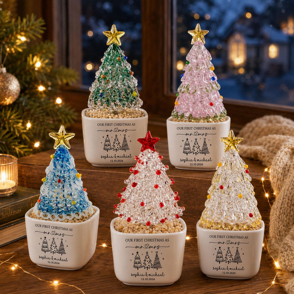 May include: Five decorative tabletop Christmas trees in white ceramic pots. Each tree features a colored star topper and small beads. The pots are printed with 'OUR FIRST CHRISTMAS AS mr & mrs', 'SOPHIA & MICHAEL', and the date '12.10.2026'.