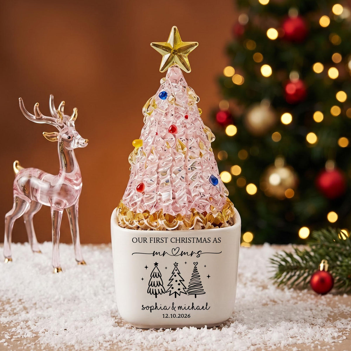 May include: A glass Christmas tree figurine with a gold star topper and colorful accents, set in a white ceramic pot. The pot features black text reading "OUR FIRST CHRISTMAS AS mr & mrs", "sophia & michael", and "12.10.2026" with tree icons.