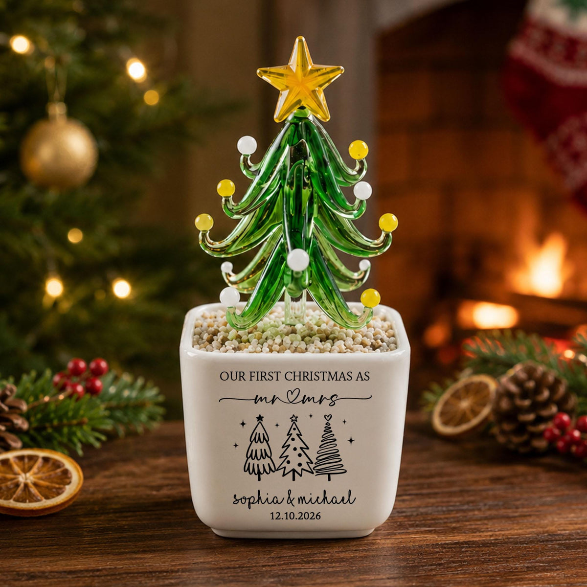 May include: A glass Christmas tree ornament with a yellow star topper and small white and yellow glass spheres on its branches. The tree is set in a white square ceramic planter with the text "OUR FIRST CHRISTMAS AS mr & mrs", "sophia & michael", and "12.10.2026" printed on the front.