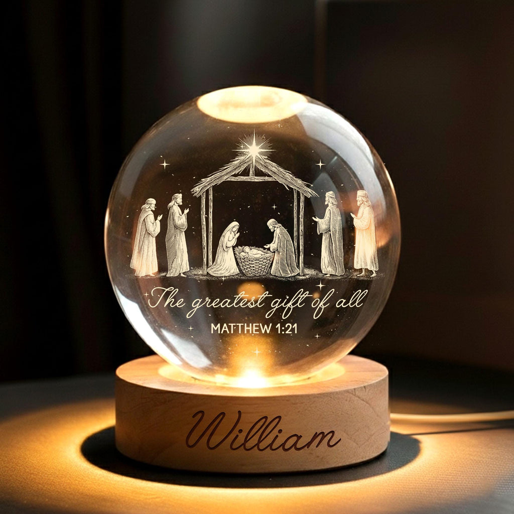 May include: A clear glass sphere featuring a laser-etched nativity scene with figures, a stable, and a star. The text reads "The greatest gift of all" and "MATTHEW 1:21". The sphere rests on a round wooden base with the name "William" engraved.