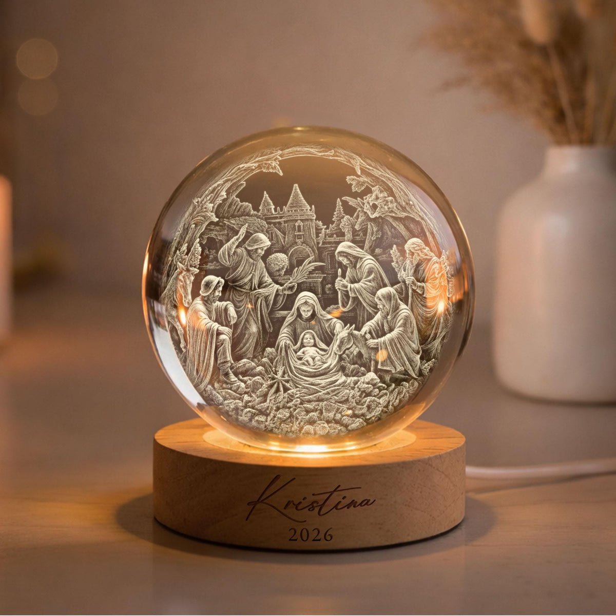 May include: A clear glass sphere featuring a 3D laser-engraved nativity scene with figures and a building, illuminated by a circular wooden base. The base is engraved with the name Kristina and the year 2026 in a dark script and serif font.