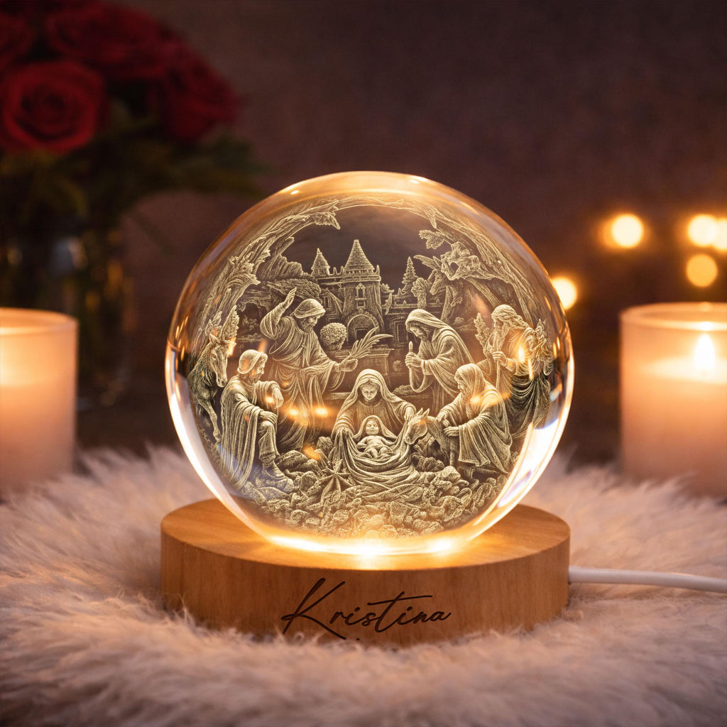 May include: A clear glass sphere featuring an intricate 3D laser-engraved nativity scene with figures of the holy family and animals. The sphere rests on a circular light-colored wooden base with the name Kristina engraved in black script.