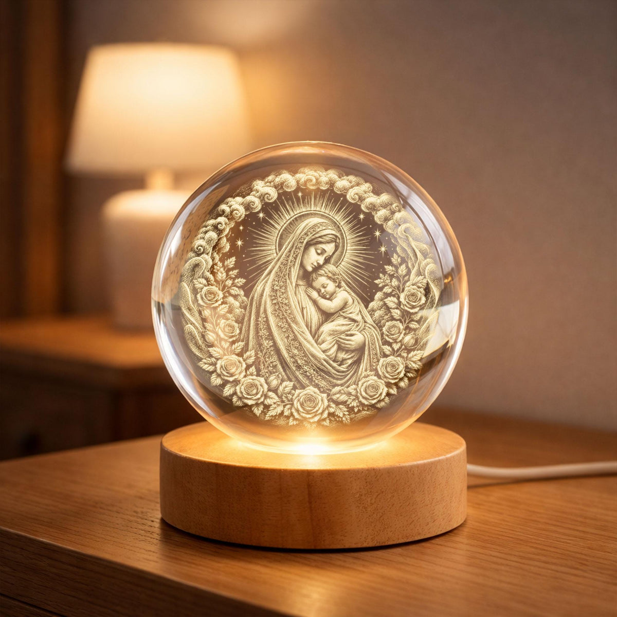 May include: A clear glass sphere featuring an internal laser-etched engraving of a figure holding a child, surrounded by a circular wreath of roses and clouds. The sphere rests on a cylindrical light-colored wooden base with an integrated light.