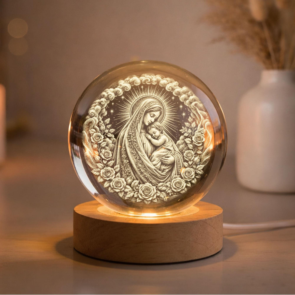May include: A spherical glass ornament featuring an internal laser-etched depiction of a woman holding a child, surrounded by a circular wreath of roses and clouds. The glass sphere rests on a cylindrical light-colored wooden base with internal illumination.