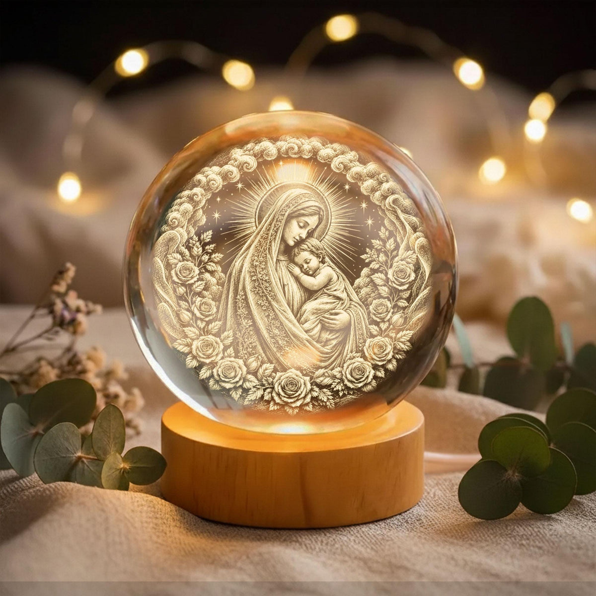May include: A clear glass sphere featuring an internal laser-etched engraving of a woman holding a child, surrounded by a circular frame of roses. The sphere is mounted on a cylindrical light-colored wooden base that illuminates the design.