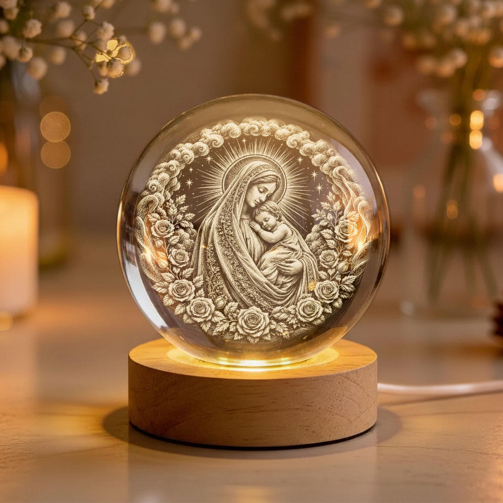 May include: A clear glass sphere featuring an intricate 3D laser-etched engraving of a mother holding a child, surrounded by a circular wreath of roses and clouds. The sphere rests on a cylindrical light-colored wooden base with an internal light.