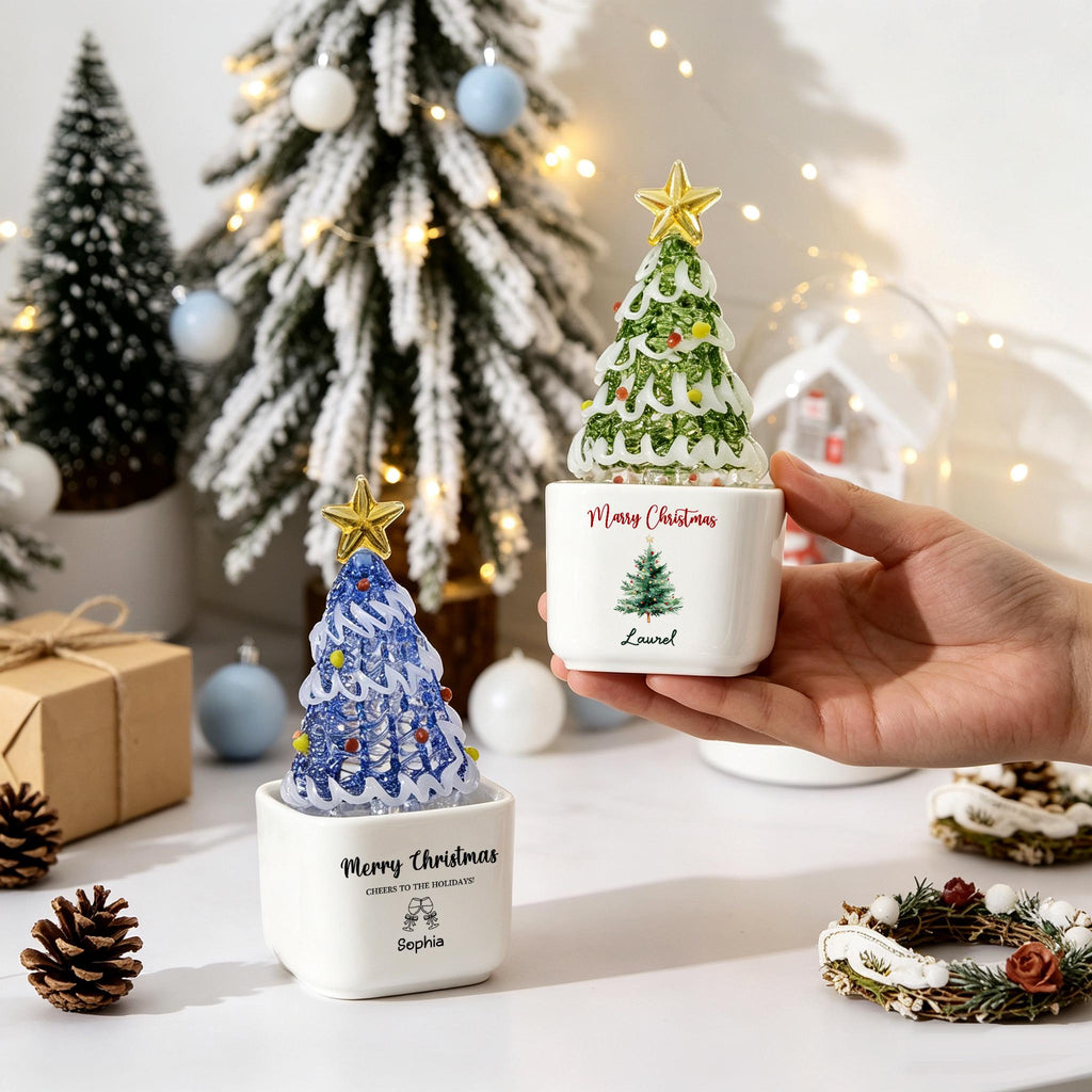 May include: Two white ceramic square planters featuring glass Christmas tree ornaments with gold stars. One planter displays the text Merry Christmas, Cheers to the Holidays, and the name Sophia. The other shows Merry Christmas and Laurel.