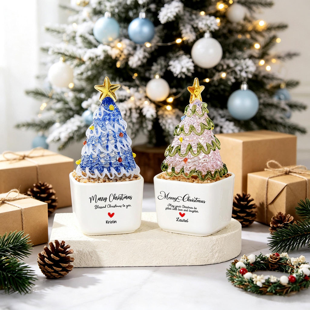 May include: Two decorative tabletop Christmas trees in white square ceramic pots. One tree is blue with white swirls and a gold star, labeled 'Merry Christmas' and 'Kristin'. The other is pink with green swirls and a gold star, labeled 'Merry Christmas' and 'Laurel'.