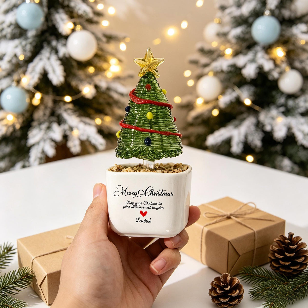 May include: A green glass Christmas tree ornament with a yellow star topper and colorful glass beads, set in a white ceramic pot. The pot features the text "Merry Christmas, May your Christmas be filled with love and laughter, Laurel" with a red heart.