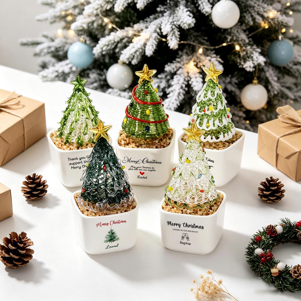 May include: Five miniature Christmas tree ornaments in white square ceramic pots. Each tree features a gold star topper and unique wire or glass designs. The pots display printed text including Merry Christmas and names like Laurel and Sophia.