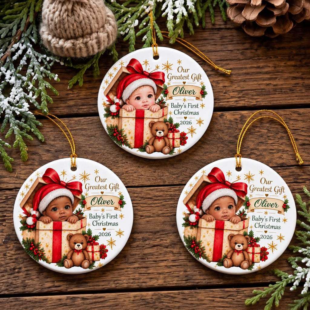 May include: Three round white ceramic ornaments featuring a baby in a Santa hat inside a gift box with a teddy bear. The text reads Our Greatest Gift, Oliver, Baby's First Christmas, and 2026. Each ornament has a gold hanging string.