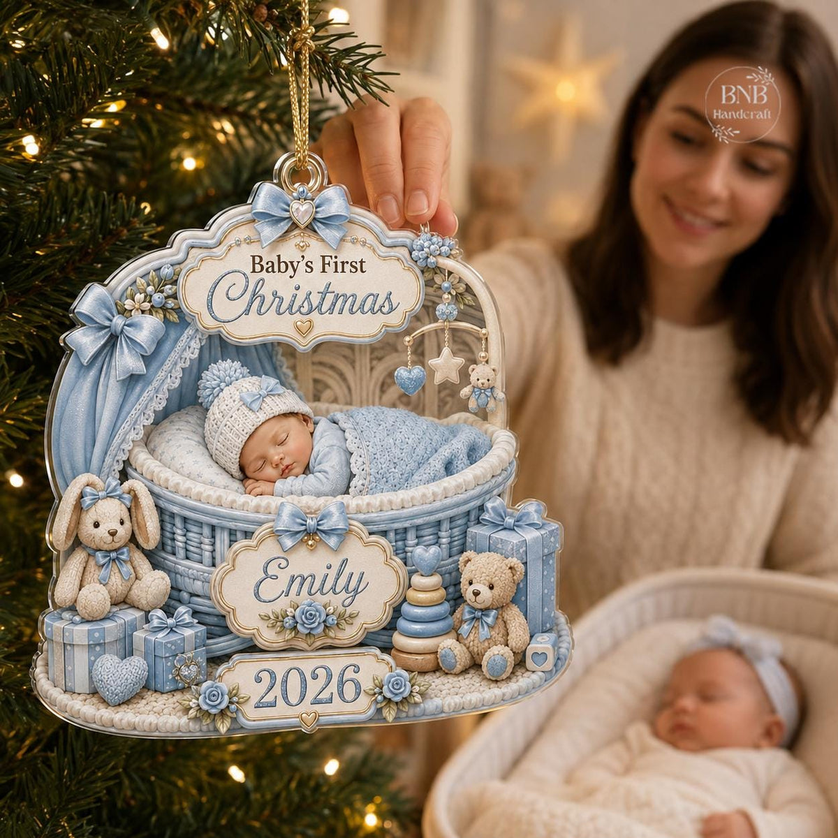 May include: A decorative Baby's First Christmas ornament featuring a sleeping infant in a blue wicker cradle. The ornament includes a teddy bear, a bunny, gift boxes, and the name Emily with the year 2026 printed on ornate plaques.