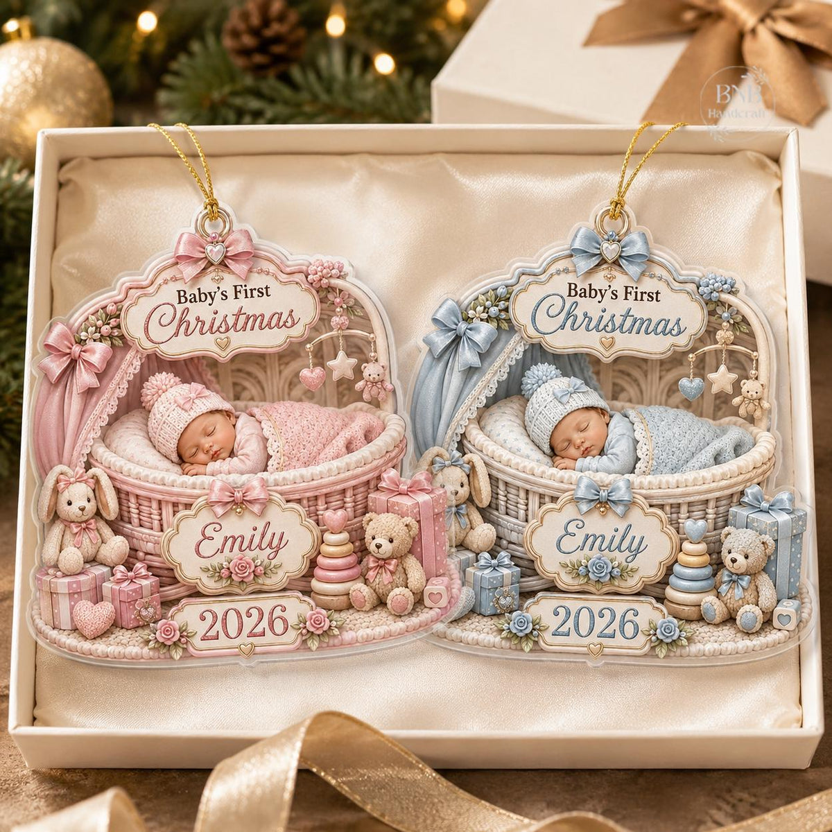 May include: Two Baby's First Christmas ornaments in a gift box. One is pink with a sleeping baby in a bassinet, a teddy bear, and the name Emily with 2026. The other is blue with a sleeping baby in a bassinet, a teddy bear, and the name Emily with 2026.