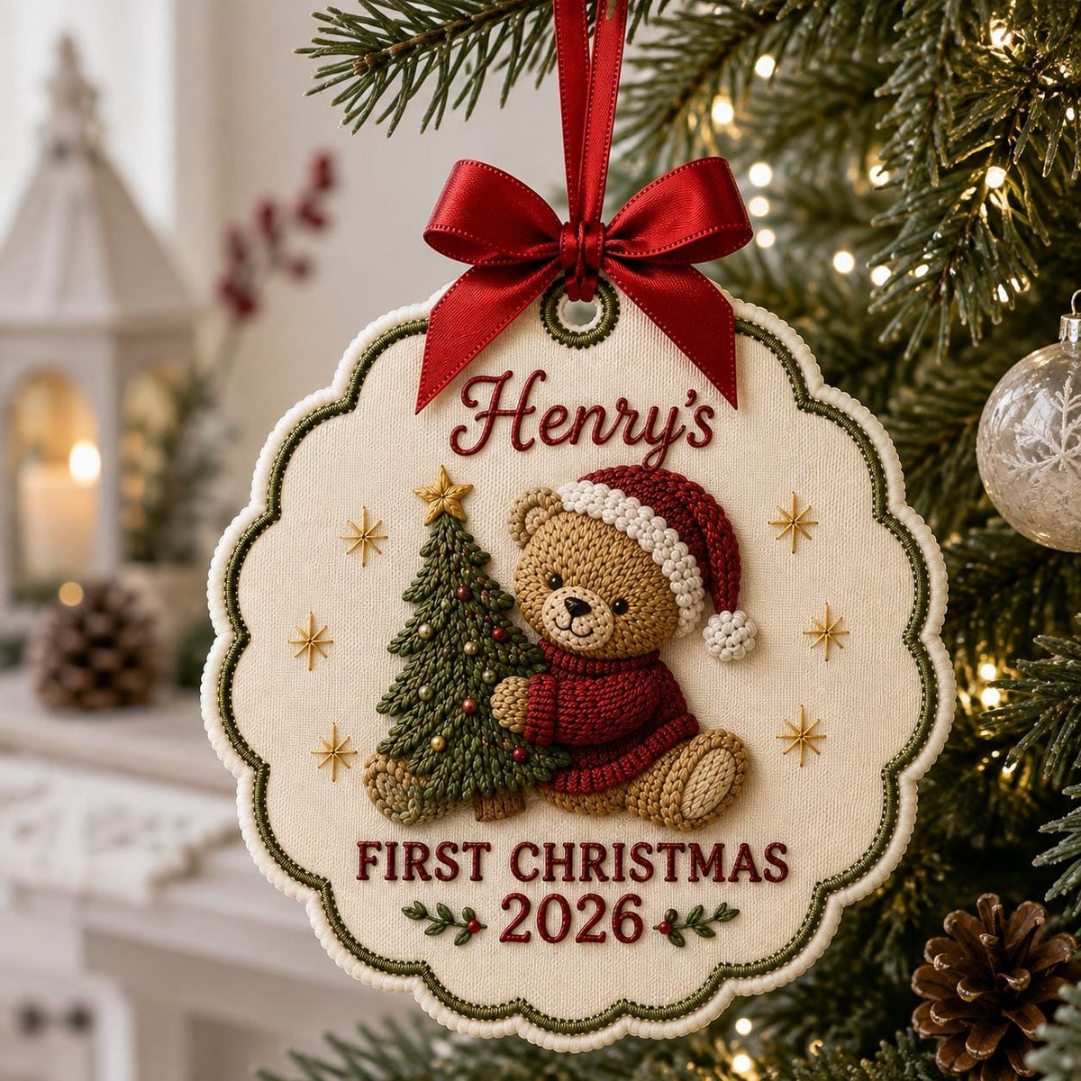 May include: A scalloped, cream-colored fabric Christmas ornament featuring an embroidered brown teddy bear in a red sweater and Santa hat holding a green Christmas tree. The text reads Henry's FIRST CHRISTMAS 2026. It has a red satin ribbon bow.