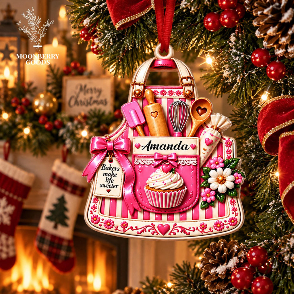 May include: A decorative Christmas ornament shaped like a pink and white striped apron. It features a pocket with the name Amanda, a cupcake, a whisk, a rolling pin, a spatula, a wooden spoon, and a tag reading Bakers make life sweeter.