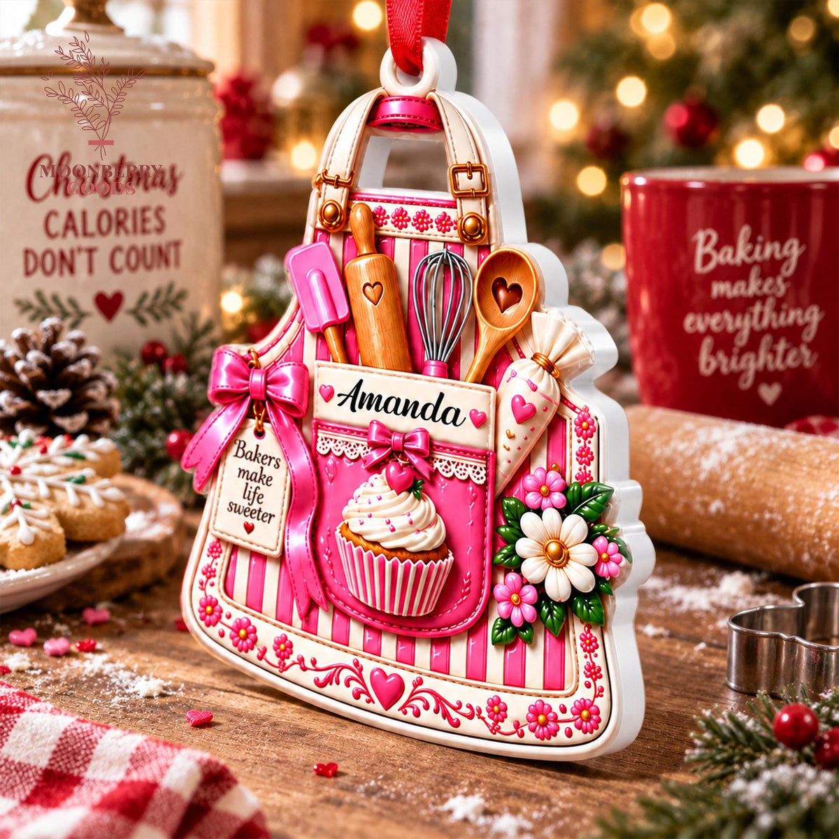 May include: A white and pink striped apron-shaped ornament featuring a pocket with the name Amanda, a cupcake graphic, and kitchen tools including a rolling pin, whisk, and spatula. A tag reads Bakers make life sweeter, with floral accents.