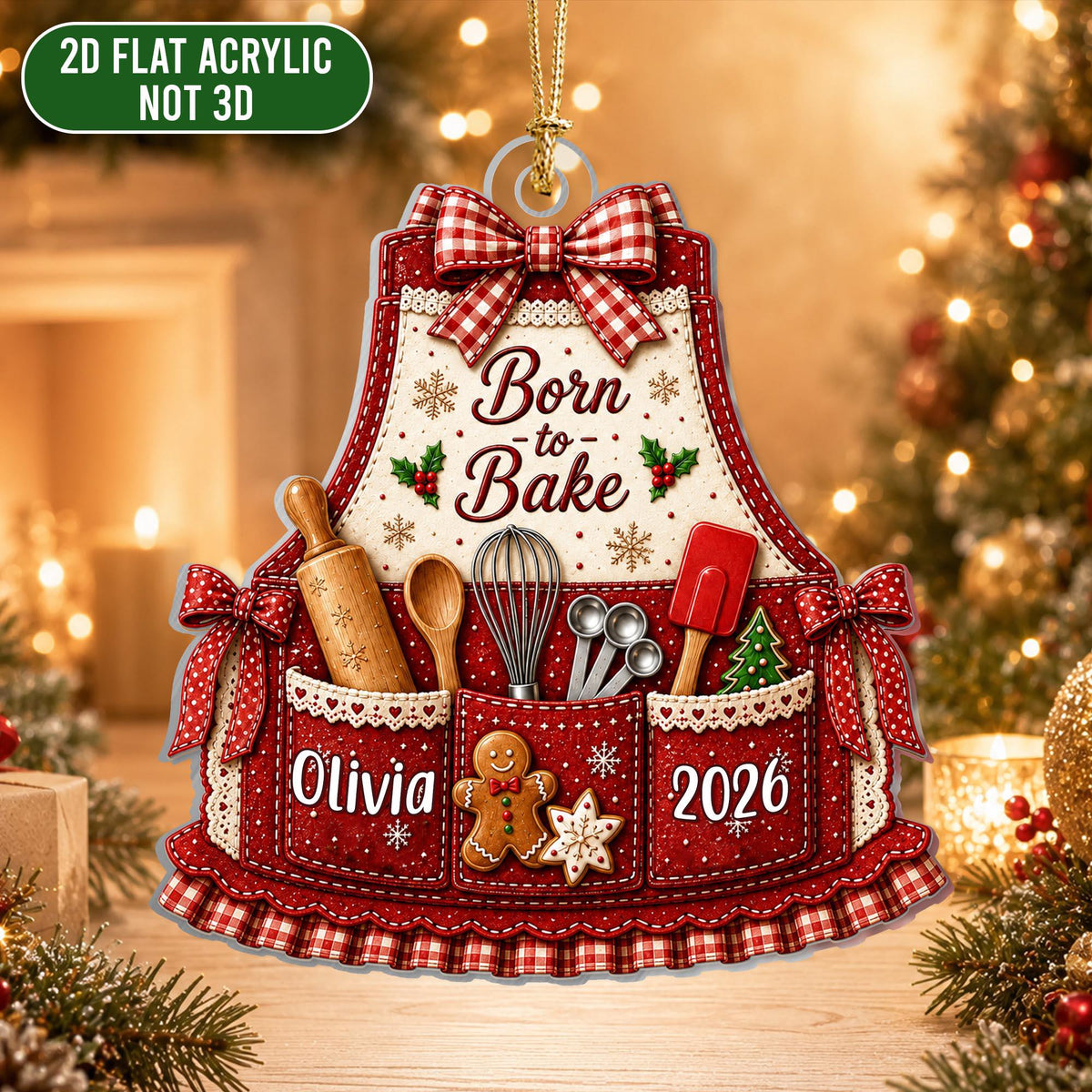 May include: A 2D flat acrylic ornament shaped like an apron with a red and white gingham bow, featuring the text Born to Bake, a rolling pin, whisk, measuring spoons, spatula, a gingerbread man, the name Olivia, and the year 2026.