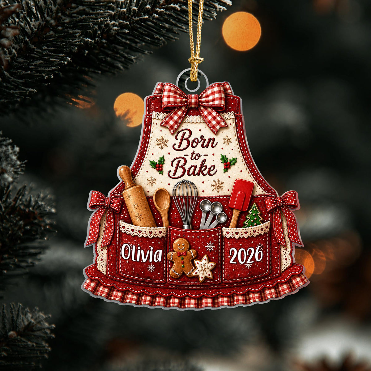 May include: A decorative apron-shaped Christmas ornament featuring the text Born to Bake, a red and white gingham bow, and illustrations of a rolling pin, whisk, and spatula. The pockets display the name Olivia and the year 2026 with a gingerbread man.