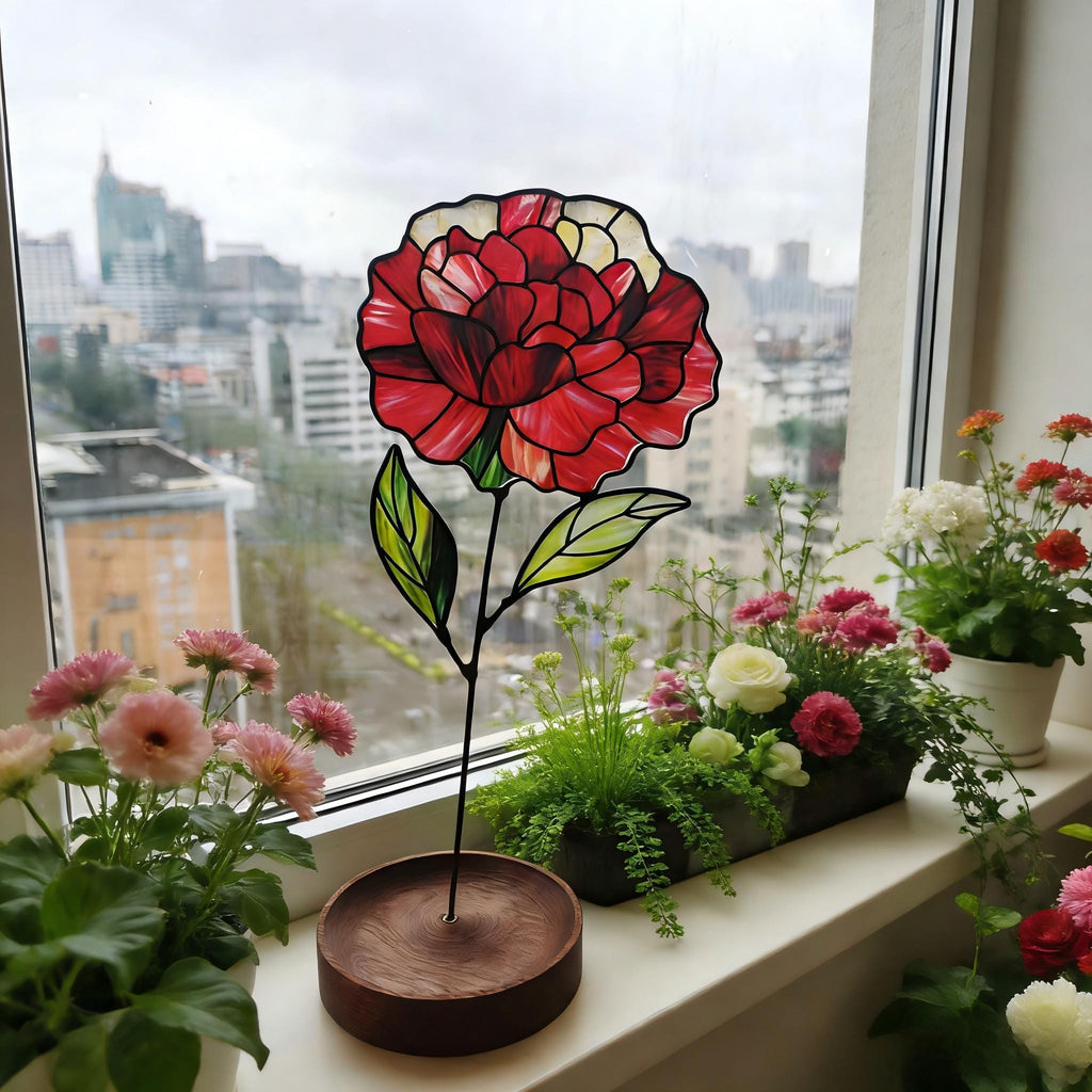 May include: A stained glass flower ornament featuring a large, multi-toned red and white peony bloom with green leaves, supported by a thin black metal stem attached to a circular, dark brown wooden base, displayed as a decorative piece.
