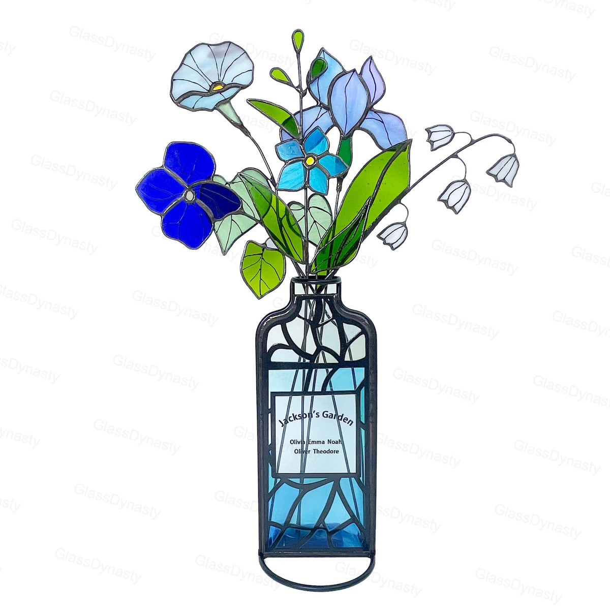 May include: Stained glass floral arrangement in a blue vase. The bouquet features blue, purple, and white flowers with green leaves. The vase has a black frame and a label that reads "Jackson's Garden".
