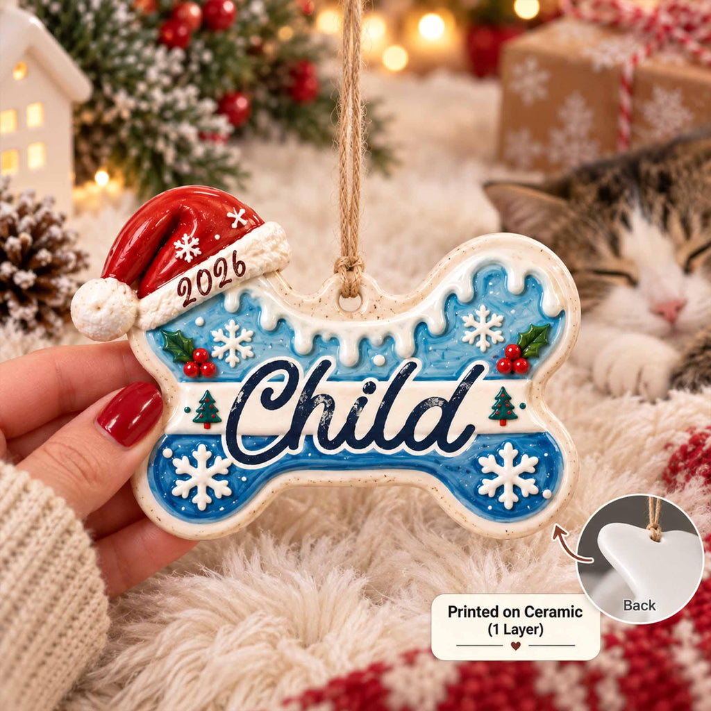May include: A bone-shaped ceramic Christmas ornament featuring a blue background with white snowflakes, green trees, and red berries. The word Child is printed in dark blue script. A red Santa hat with the year 2026 is attached to the top left.