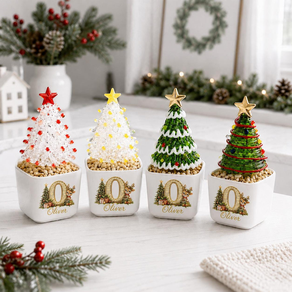 May include: Four miniature Christmas tree decorations in square white ceramic pots. Each pot features a gold letter O, a reindeer, and the name Oliver. The trees are made of wire and beads in white, green, and red, topped with gold or red stars.