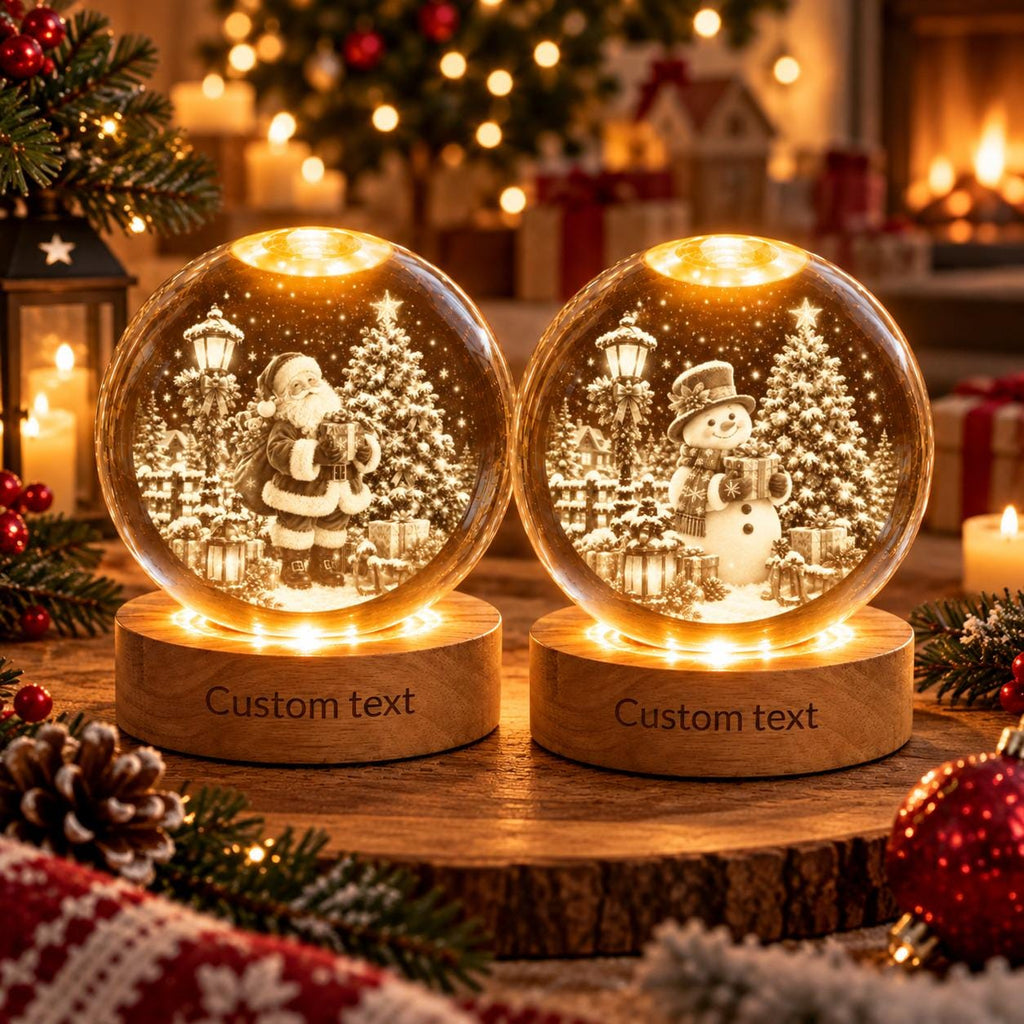May include: Two spherical glass snow globes with warm internal lighting, each resting on a circular wooden base engraved with the words Custom text. One globe features a Santa Claus figure, while the other contains a snowman, both in snowy scenes.