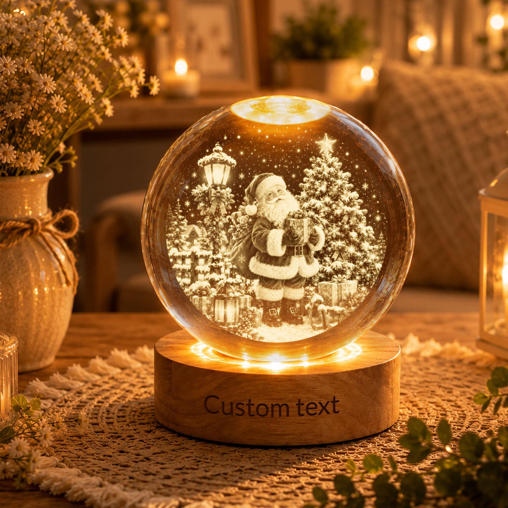 May include: A spherical glass ornament featuring an internal 3D laser-etched scene of Santa Claus standing near a Christmas tree and a street lamp. The glass sphere rests on a circular wooden base with the engraved text Custom text.