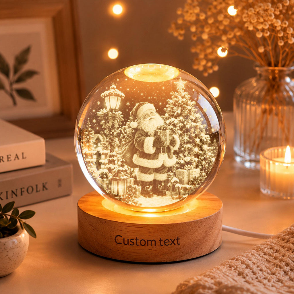 May include: A spherical glass ornament featuring an internal 3D laser-etched scene of Santa Claus standing next to a Christmas tree and a street lamp. The glass sphere rests on a circular wooden base with the engraved text Custom text.