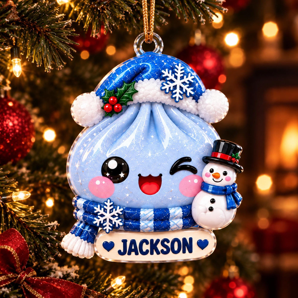 May include: A light blue dumpling ornament with a glittery finish, wearing a blue Santa hat with a snowflake and a blue striped scarf. It features a winking face, a small snowman, and a white name tag with the text JACKSON and two blue hearts.