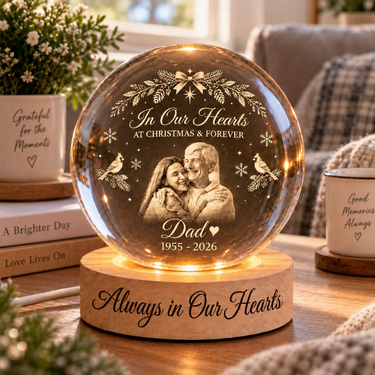 May include: A spherical glass ornament on a round wooden base featuring an engraved image of two people embracing. The glass displays the text In Our Hearts AT CHRISTMAS & FOREVER, Dad, 1955-2026, and cardinal birds. The wooden base reads Always in Our Hearts.