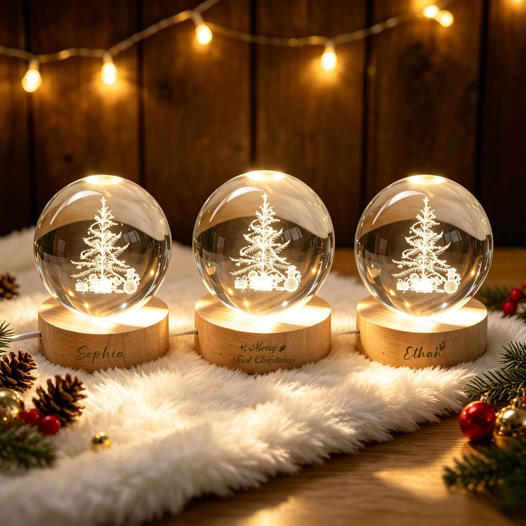 May include: Three spherical glass ornaments featuring an etched Christmas tree design, each mounted on a circular light-up wooden base. The bases are engraved with the names Sophia and Ethan, and the phrase Merry First Christmas.