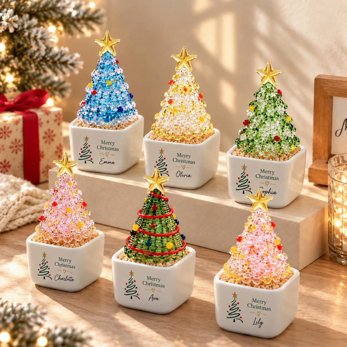 May include: Six small, conical Christmas tree ornaments in white square ceramic pots. Each tree is made of colorful beads and topped with a gold star. The pots feature the text Merry Christmas, a small tree graphic, and a unique name: Emma, Olivia, Sophia, Charlotte, Ava, or Lily.