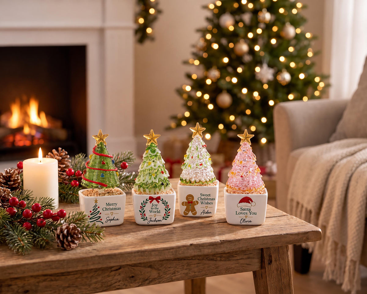 May include: Four small, square white ceramic planters, each topped with a decorative miniature Christmas tree. The trees are green, white, and pink with gold stars. Each planter features unique holiday text and names: Sophia, Jackson, Aiden, and Olivia.
