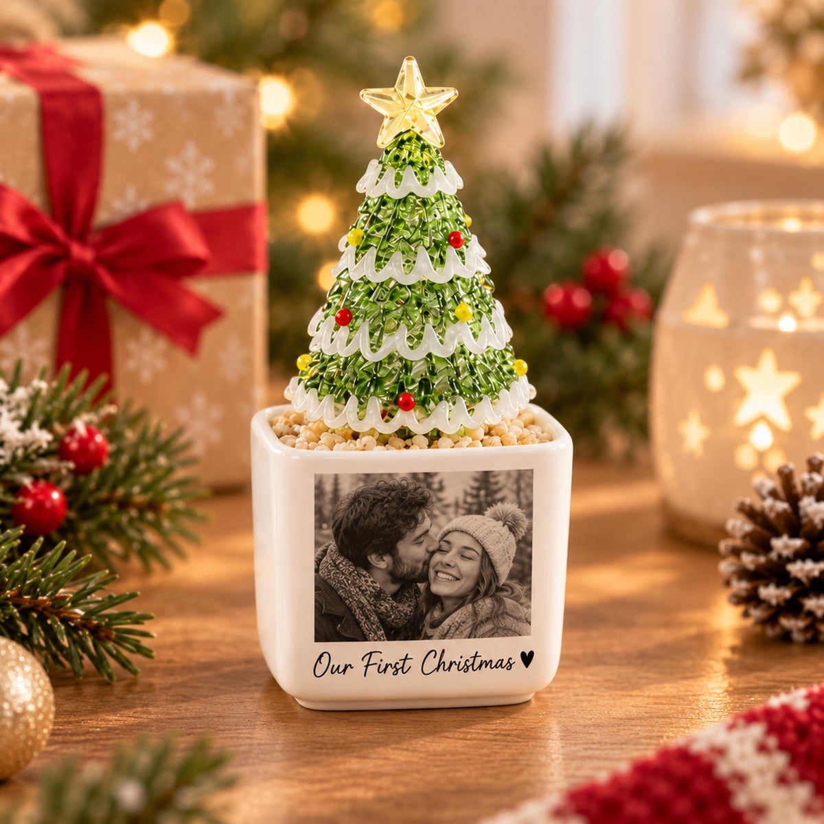 May include: A white square ceramic planter featuring a black and white photograph of a couple and the text Our First Christmas with a heart symbol. A green beaded Christmas tree with a yellow star topper sits inside the planter.