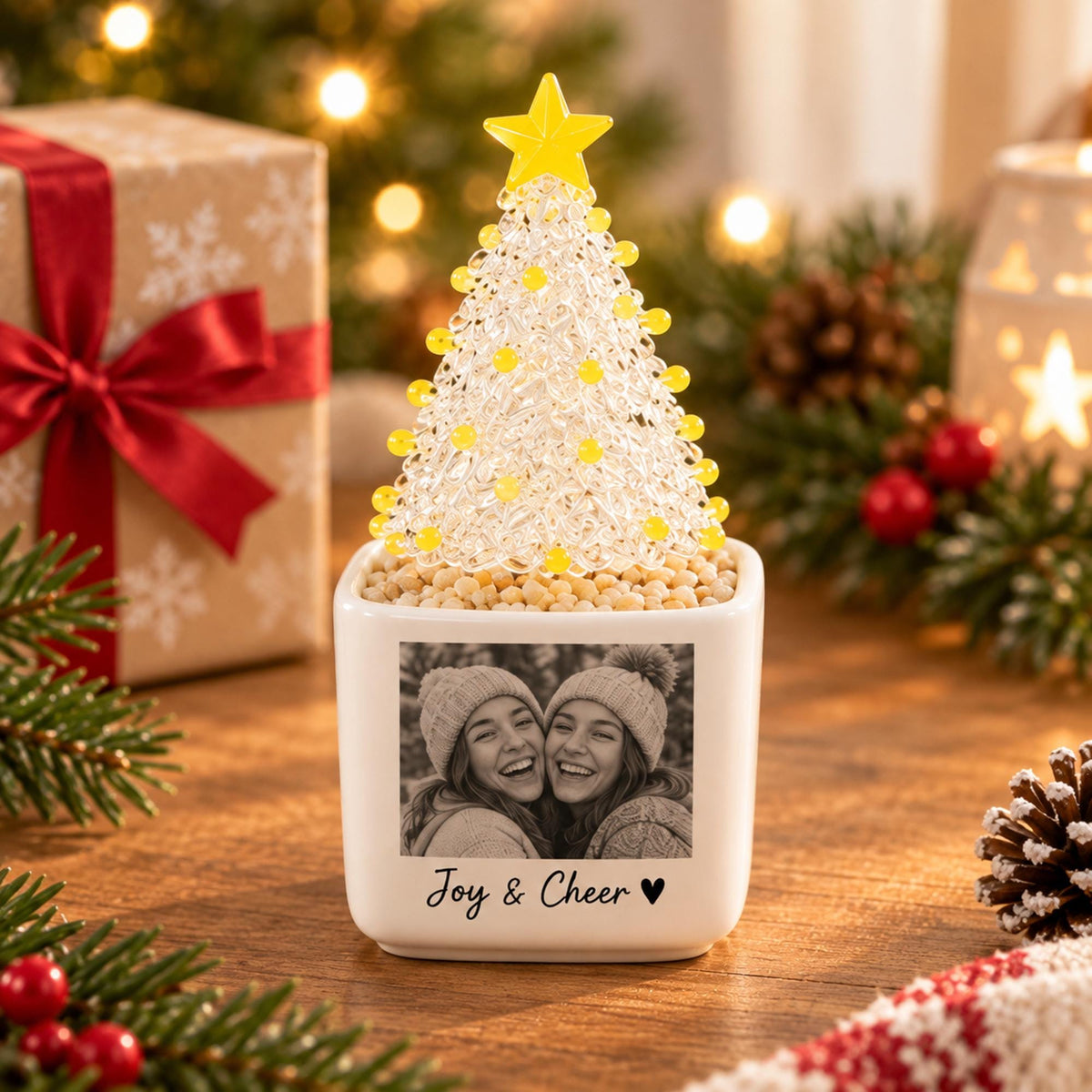 May include: A white square ceramic planter featuring a black and white photograph of two smiling people wearing beanies. Below the photo, the text reads Joy & Cheer with a heart symbol. A clear, textured Christmas tree with yellow beads sits on top.