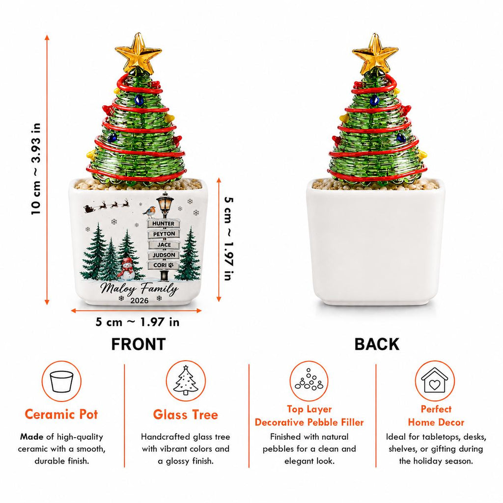 May include: A green glass Christmas tree with a gold star topper in a white ceramic pot. The pot features a printed winter scene with a signpost reading Hunter, Peyton, Jace, Judson, Cori, and Maloy Family 2026. Dimensions are 3.93 inches tall by 1.97 inches wide.