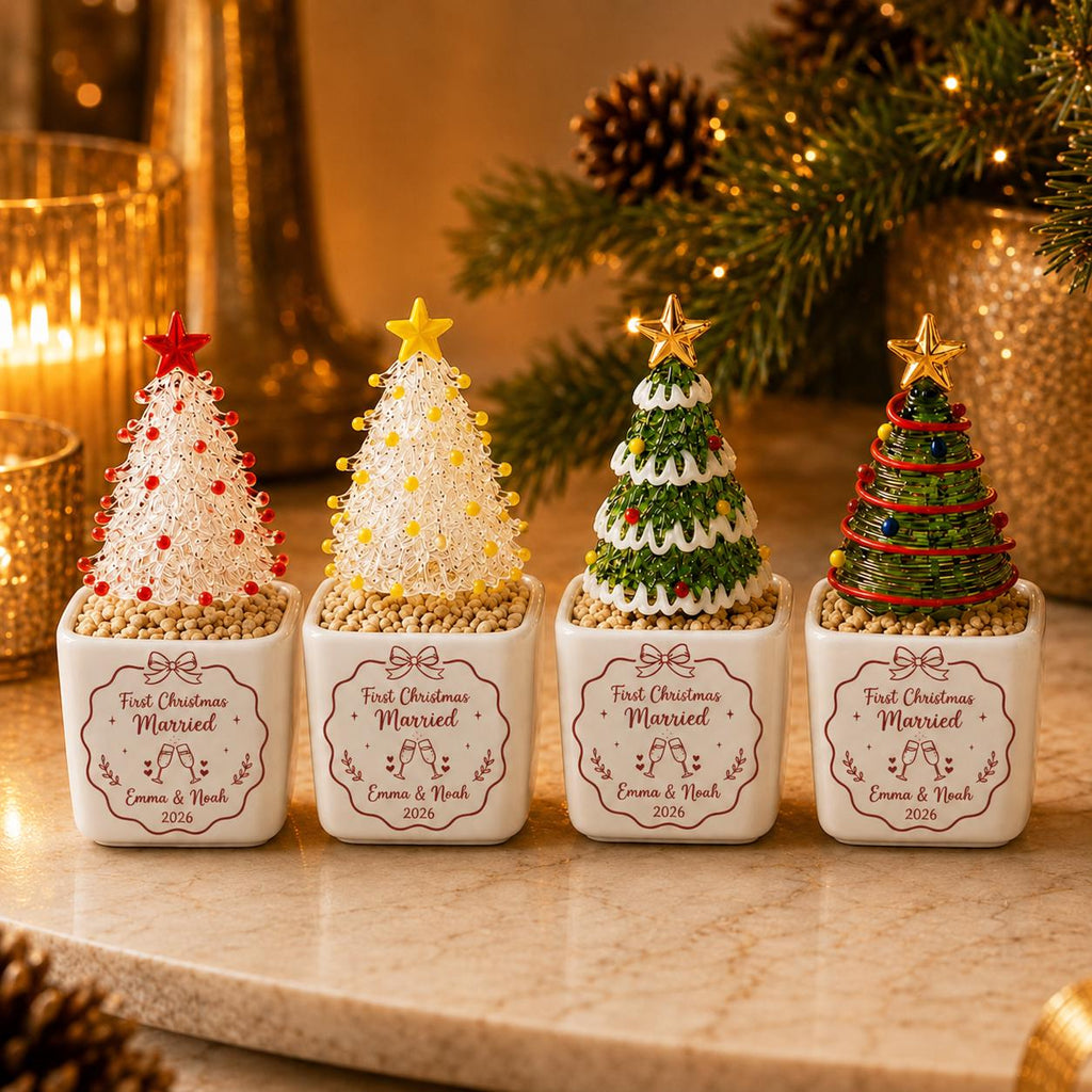 May include: Four small decorative Christmas tree ornaments in white square ceramic planters. Each planter features the text First Christmas Married, Emma & Noah, and 2026. The trees are made of wire with red, yellow, green, and gold accents.