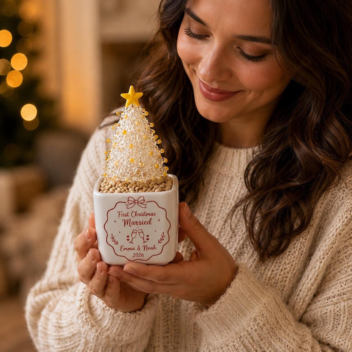 May include: A white square ceramic planter containing a small decorative tree made of clear and yellow beads topped with a yellow star. The planter features a red printed design with the text First Christmas Married, Emma & Noah, 2026.