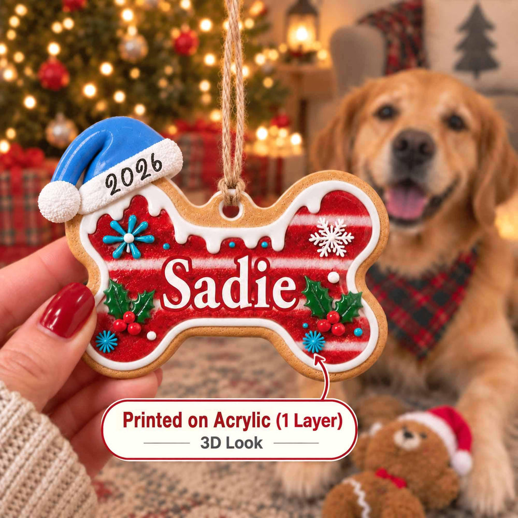 May include: A bone-shaped Christmas ornament featuring a red and white striped pattern, green holly leaves with red berries, and blue snowflake accents. The name Sadie is printed in white, with 2026 on a blue Santa hat. It hangs from a jute twine loop.