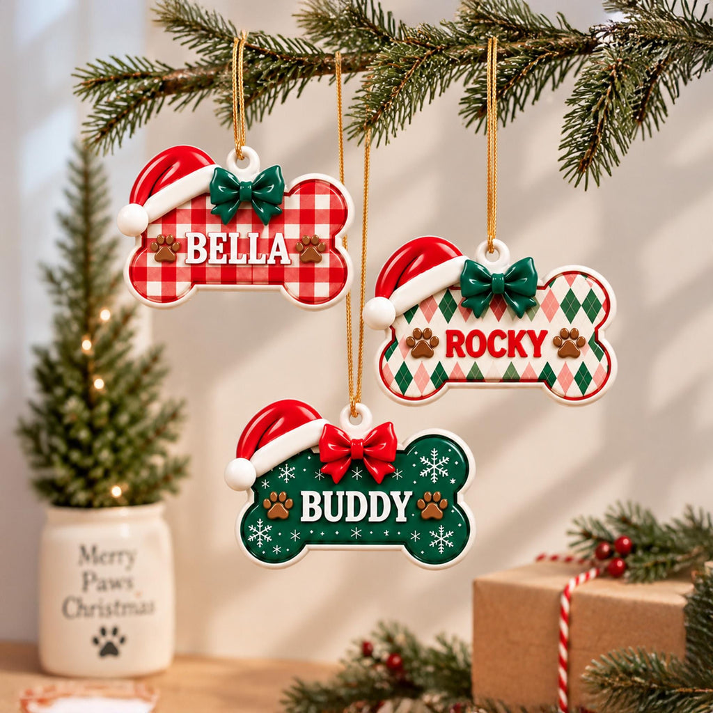May include: Three bone-shaped ornaments hanging by gold strings. The first features a red and white gingham pattern with the name BELLA. The second has a green and pink argyle pattern with the name ROCKY. The third is green with white snowflakes and the name BUDDY. Each has a Santa hat and a bow.