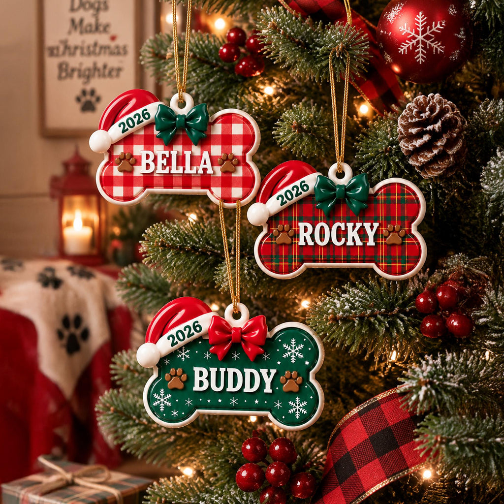 May include: Three bone-shaped Christmas ornaments hanging on a tree. Each features a Santa hat, a bow, the year 2026, and a name: Bella on a red and white gingham bone, Rocky on a red and green plaid bone, and Buddy on a green bone with snowflakes.
