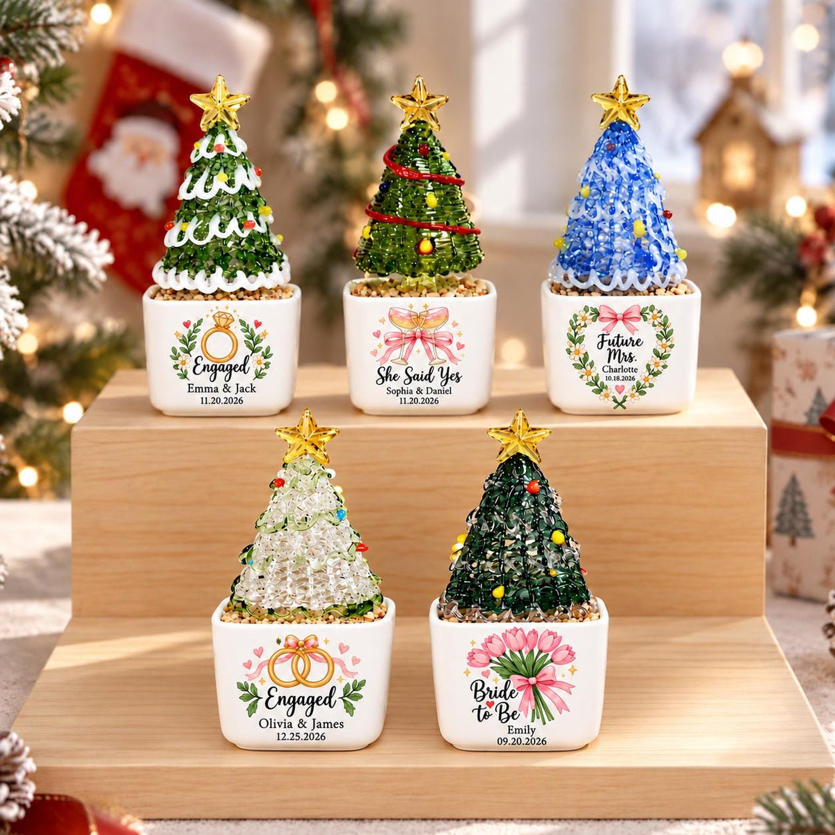 May include: Five miniature Christmas tree ornaments in white square ceramic pots. Each tree is topped with a gold star and features unique decorations, including text like Engaged, She Said Yes, Future Mrs., and Bride to Be with names and dates.