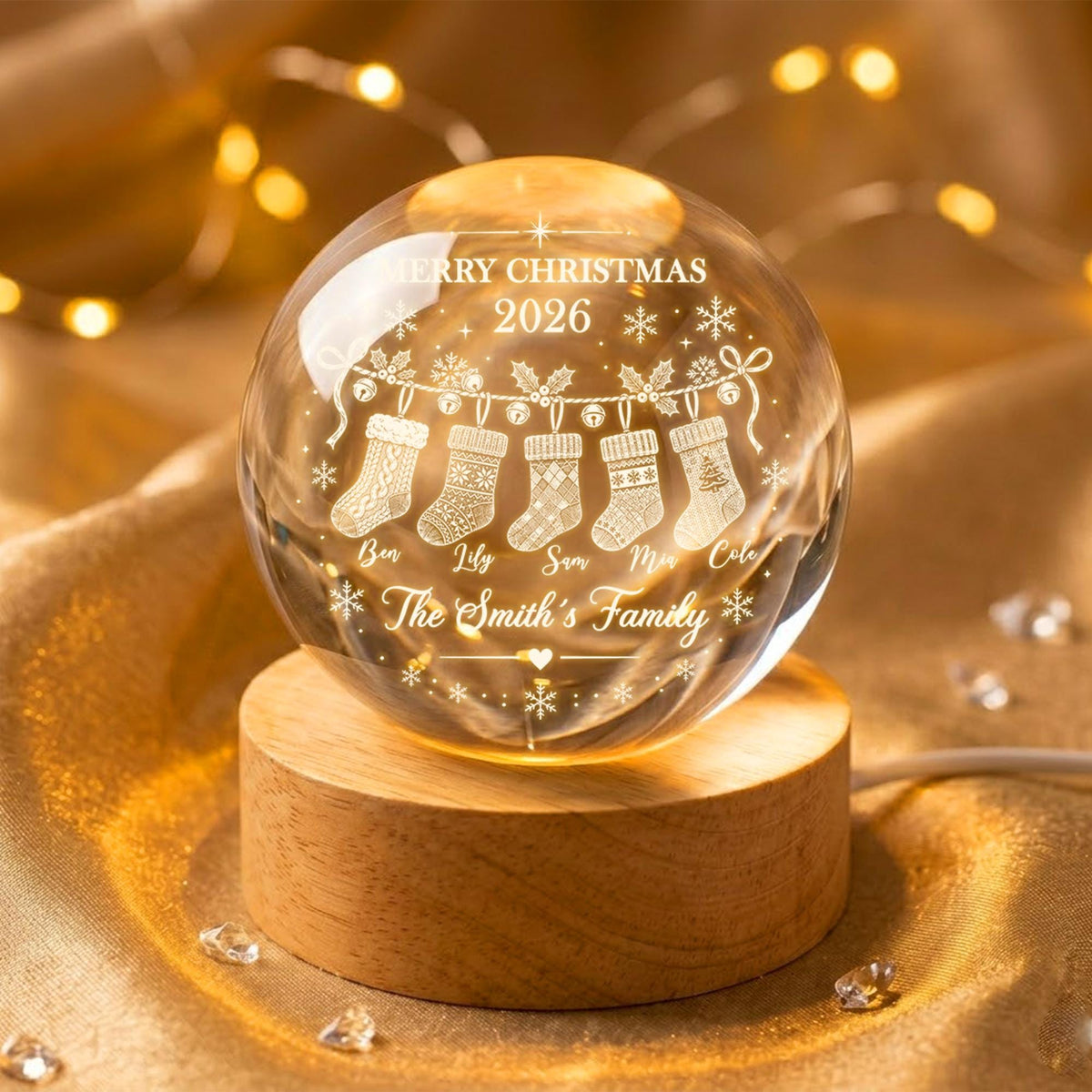 May include: A clear glass sphere ornament resting on a round wooden base. The sphere features an etched design of five hanging Christmas stockings, snowflakes, the text MERRY CHRISTMAS 2026, and the names Ben, Lily, Sam, Mia, Cole, and The Smith's Family.