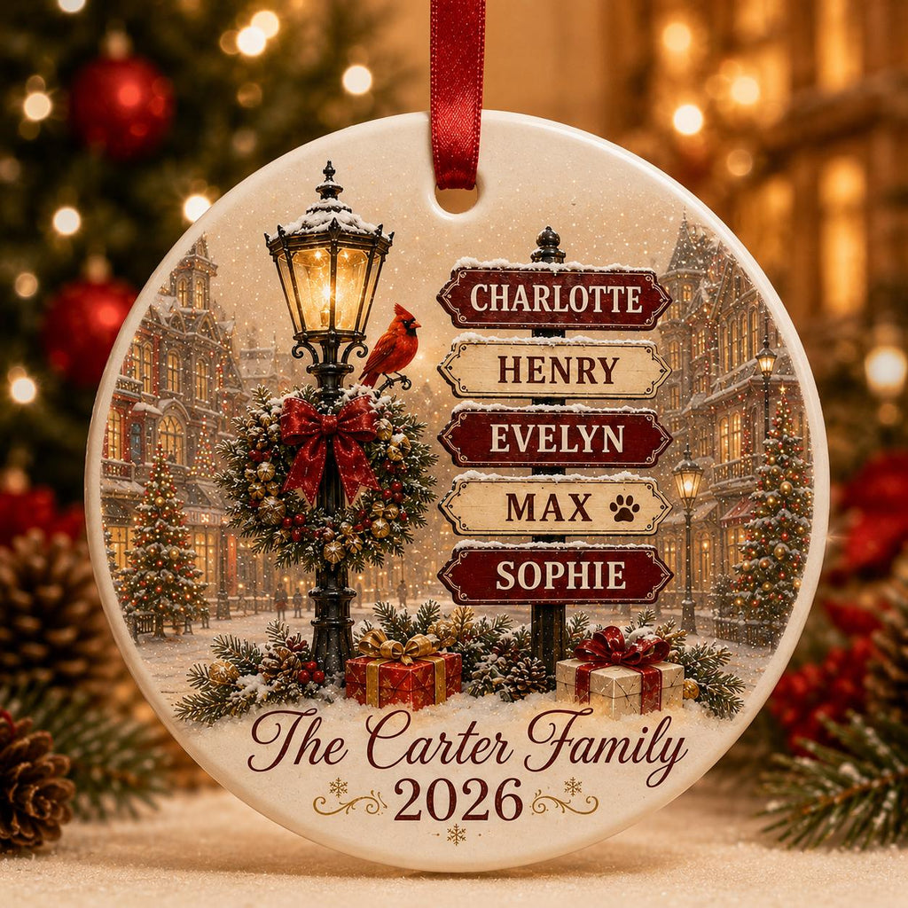 May include: A round white ceramic Christmas ornament featuring a winter street scene with a lamppost, a red cardinal, and a signpost with the names Charlotte, Henry, Evelyn, Max, and Sophie. It includes the text The Carter Family 2026.