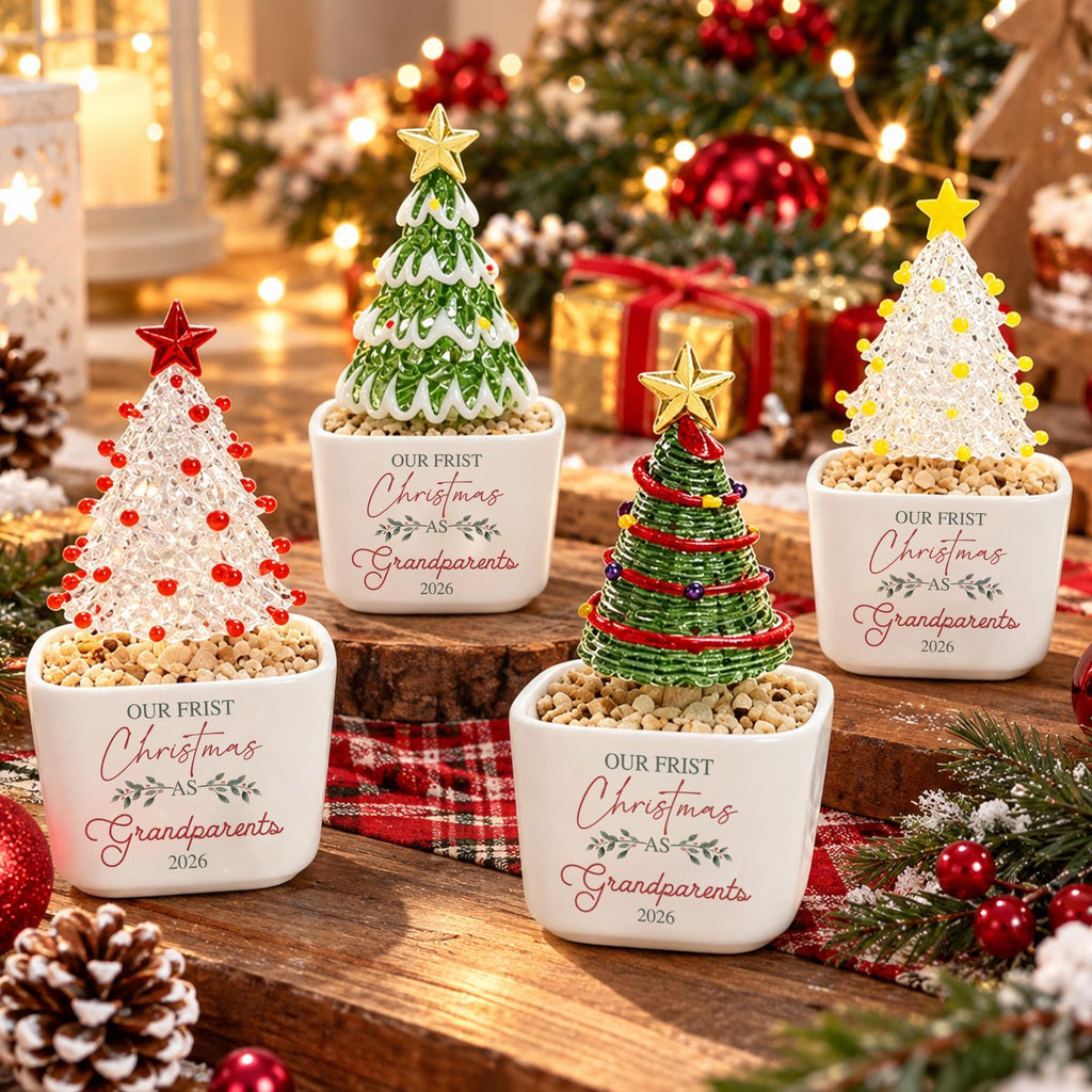 May include: Four white ceramic square planters, each containing a decorative Christmas tree ornament topped with a star. The planters feature the printed text "OUR FRIST Christmas AS Grandparents 2026" in red and grey script and block lettering.