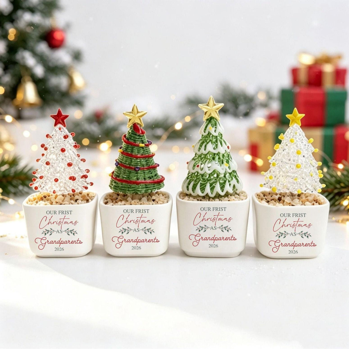 May include: Four miniature decorative Christmas trees in white square ceramic pots. Each pot features the text "OUR FRIST Christmas AS Grandparents 2026". The trees vary in color and texture, topped with gold or red stars, and sit on small pebbles.