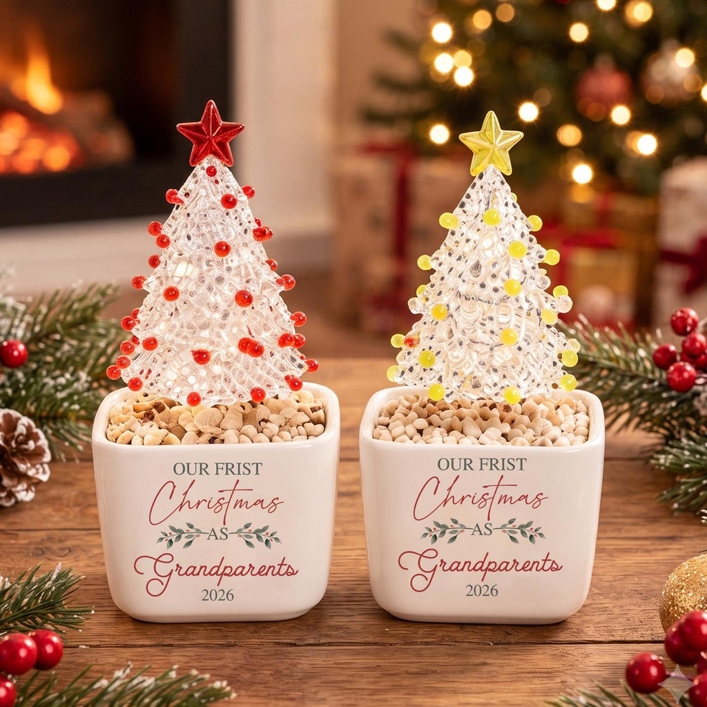 May include: Two white ceramic square planters containing clear textured Christmas tree ornaments with red and yellow beads, topped with stars. The planters feature the text "OUR FRIST Christmas AS Grandparents 2026" in red and gray script.
